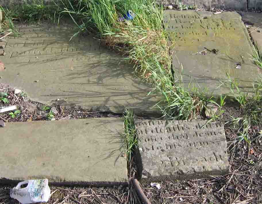 The fragment at top right (next to the squashed blue beer can) is all that is left of the memorial to the Rev. John Lowe, the 2nd Minister of Atherton Chapel, who served from 1755-1780. Photo by Peter Wood, July 2005