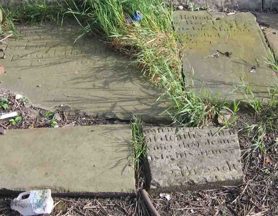 The fragment at top right (next to the squashed blue beer can) is all that is left of the memorial to the Rev. John Lowe, the 2nd Minister of Atherton Chapel, who served from 1755-1780. Photo by Peter Wood, July 2005